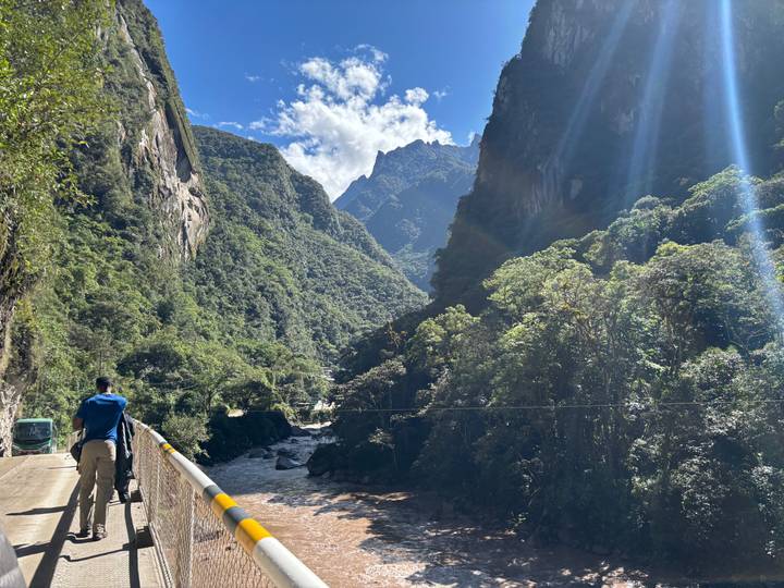 Flussschlucht mit üppiger Vegetation und Person, die über eine Brücke geht.