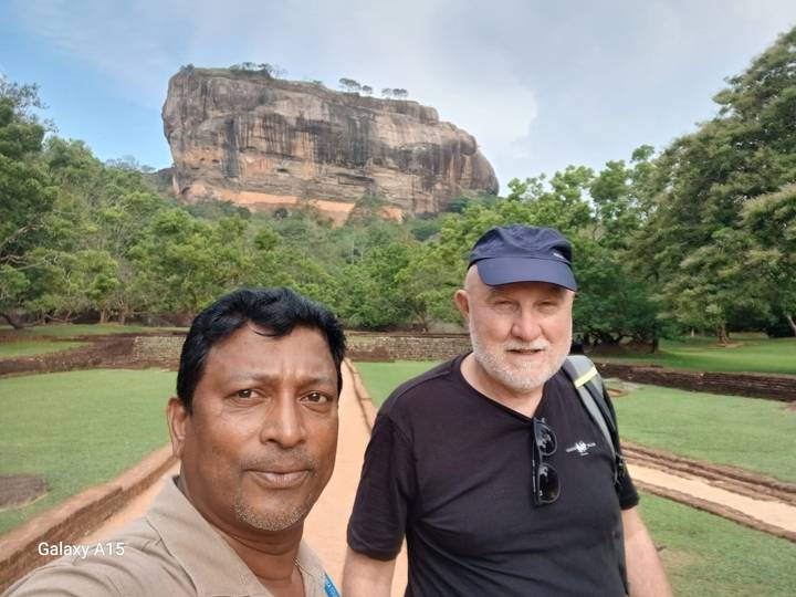 Deux hommes prenant un selfie avec la forteresse rocheuse de Sigiriya en arrière-plan.