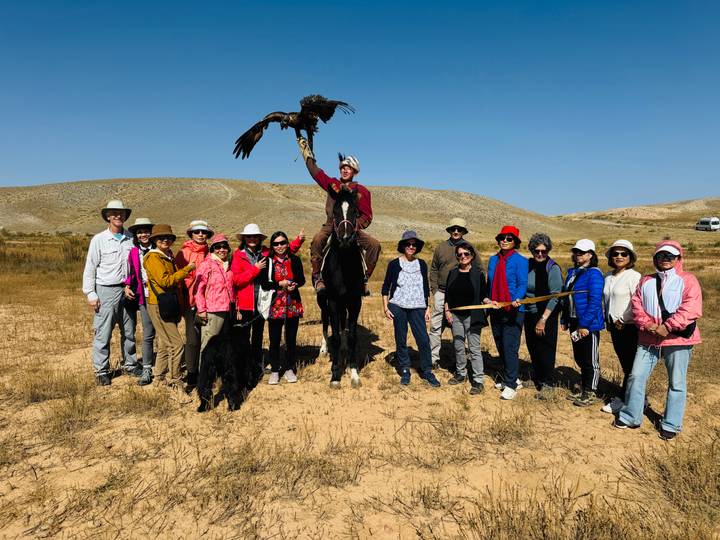 Grupo de personas y una persona a caballo sosteniendo un águila en un paisaje desértico.