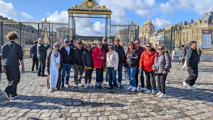 Groupe de personnes debout devant les grilles de Versailles.