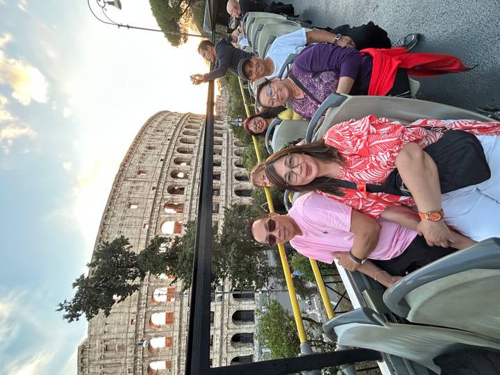 Touristes dans un bus à toit ouvert avec le Colisée en arrière-plan au coucher du soleil.