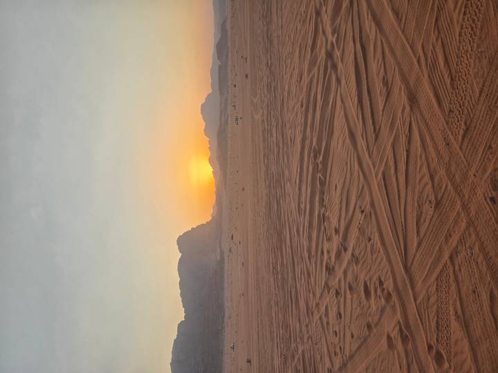 Sunset over a wide expanse of desert with tracks in the sand.