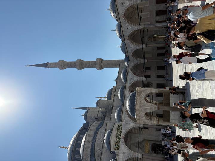 Des personnes visitant la cour d'une mosquée avec un minaret élancé.
