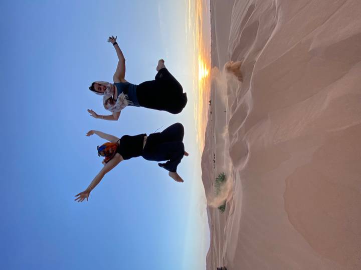 Deux femmes sautant sur une dune de sable au coucher du soleil.