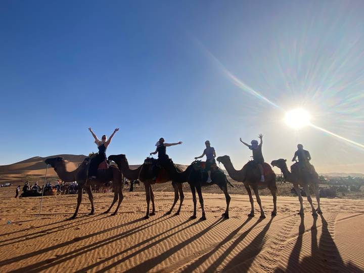 Groupe de personnes montant des chameaux sur une dune de sable.