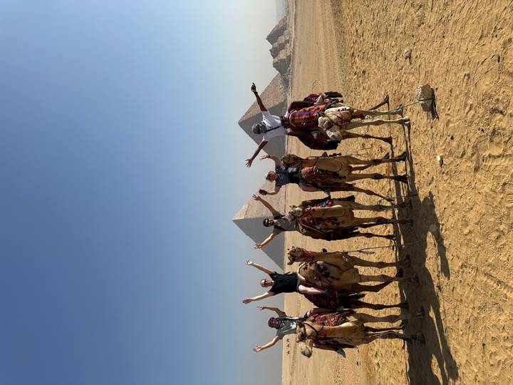 Groupe de personnes à dos de chameaux devant les pyramides.