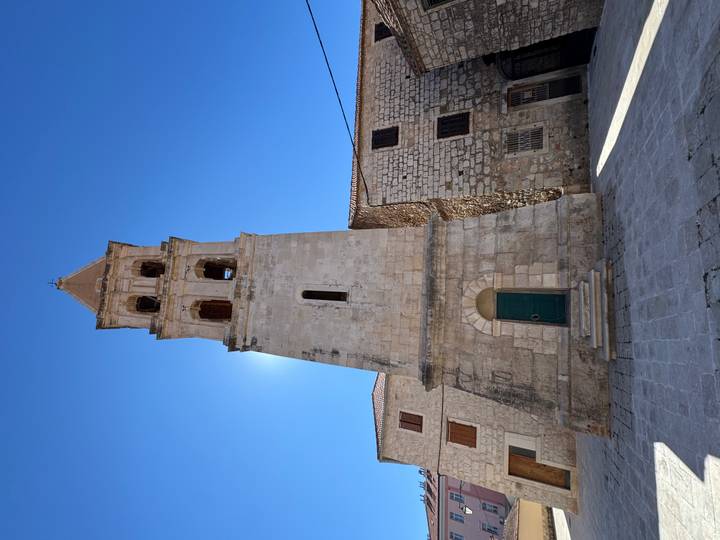 Grand clocher dans une cour de pierre sous un ciel bleu dégagé.