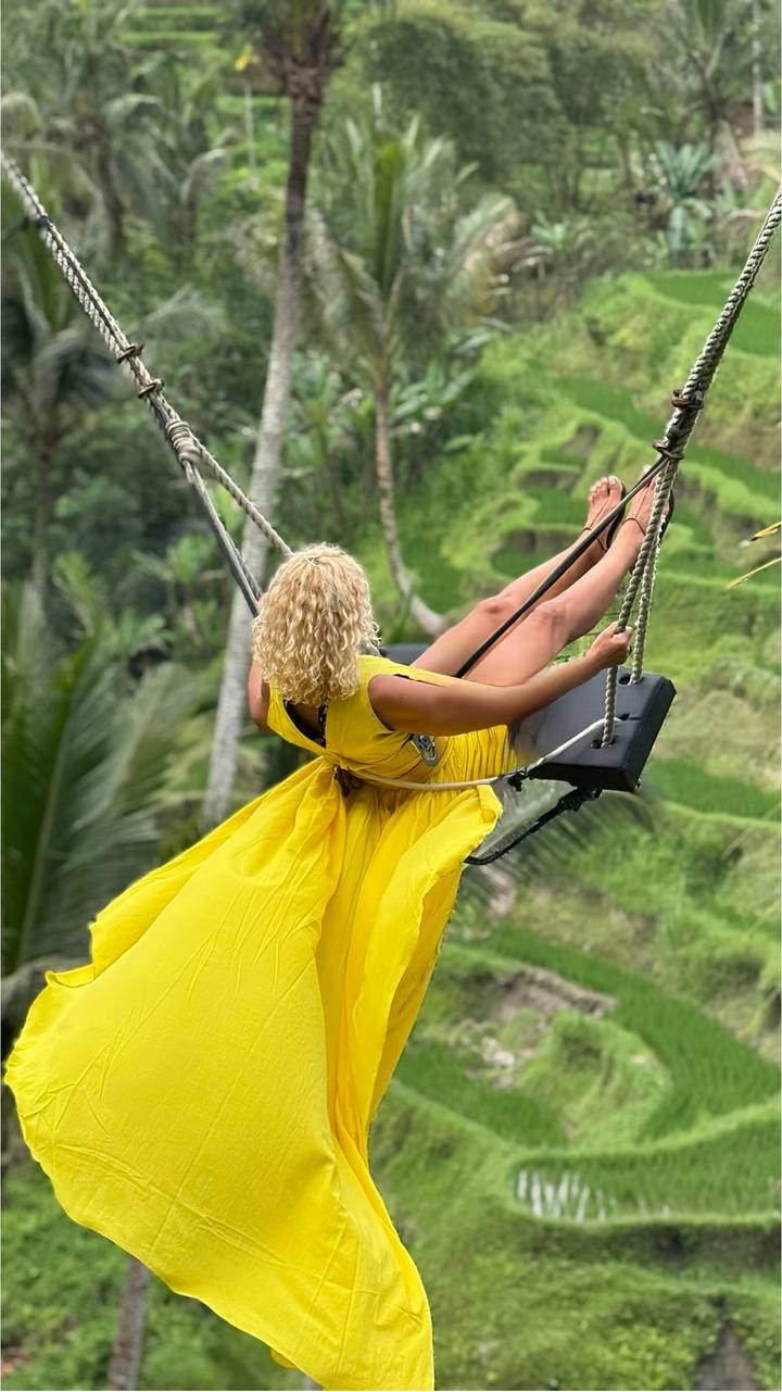 Femme en robe jaune se balançant au-dessus de luxuriantes rizières en terrasses.