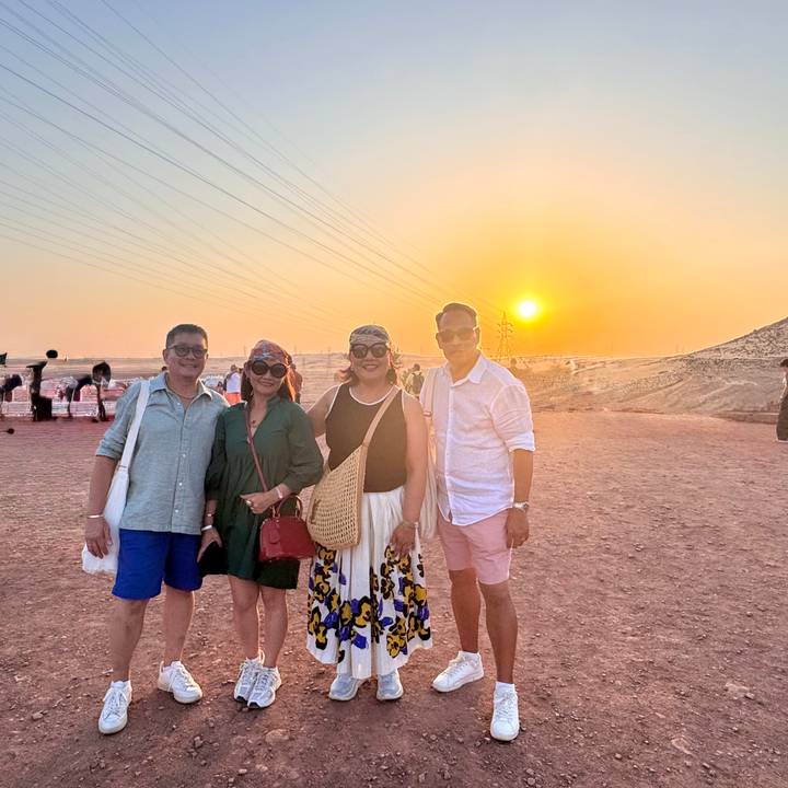 Quatre personnes posant avec un coucher de soleil sur un paysage désertique.