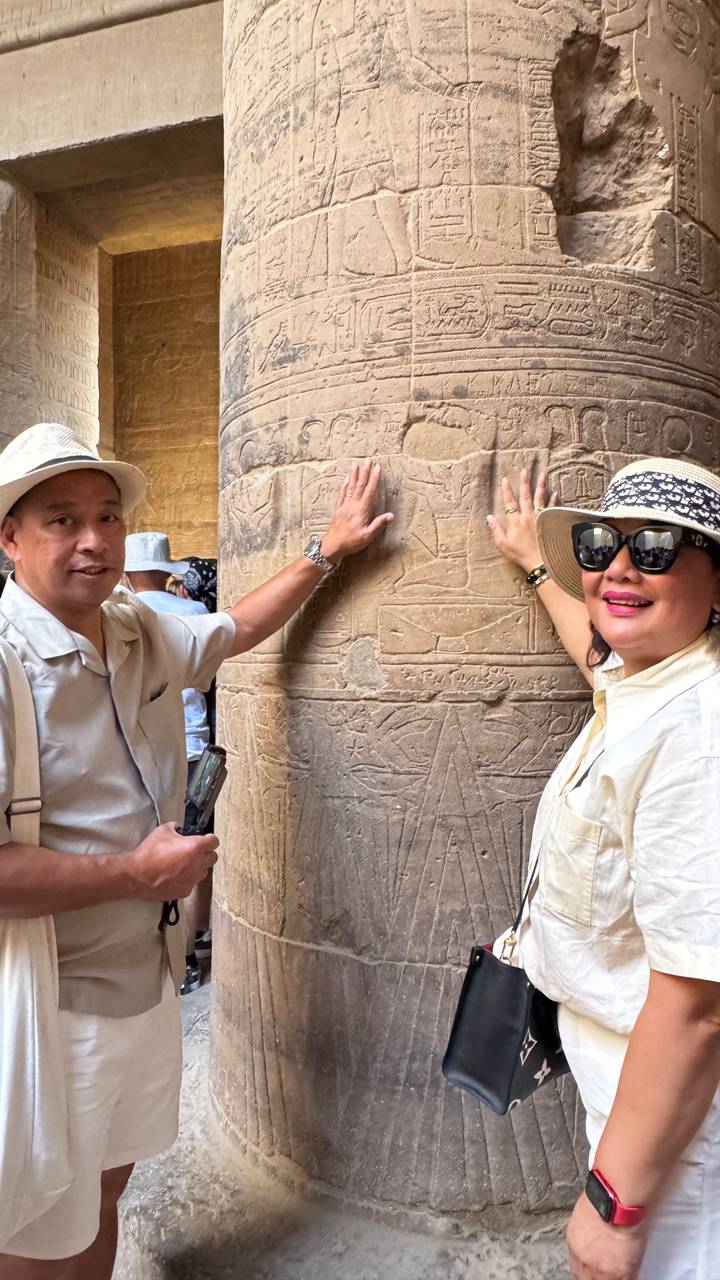 Deux personnes touchant d'anciennes gravures hiéroglyphiques sur un pilier de pierre.