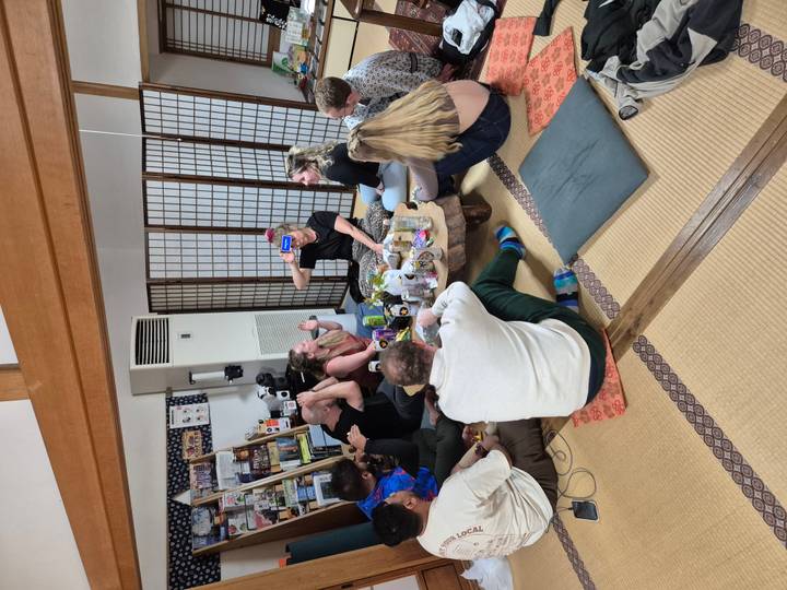 Personas sentadas alrededor de una mesa en el interior, pareciendo disfrutar de una reunión casual.