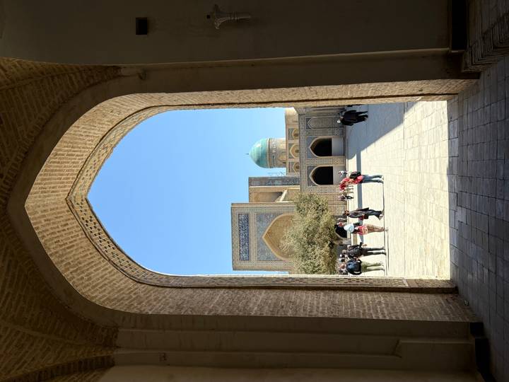 Vue d'une cour historique avec un dôme bleu à travers une porte voûtée.