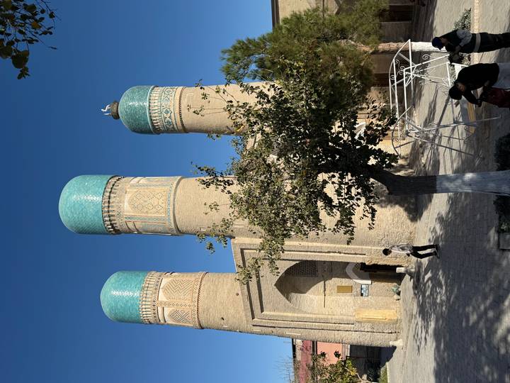 Trois minarets avec un travail de carrelage complexe et des arbres.