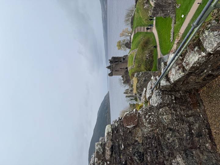 Ruines d'un château de pierre surplombant un lac avec des personnes dans la scène.