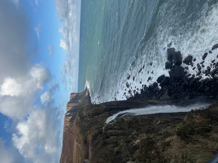 Côte spectaculaire avec de hautes falaises et une cascade qui se jette dans l'océan.