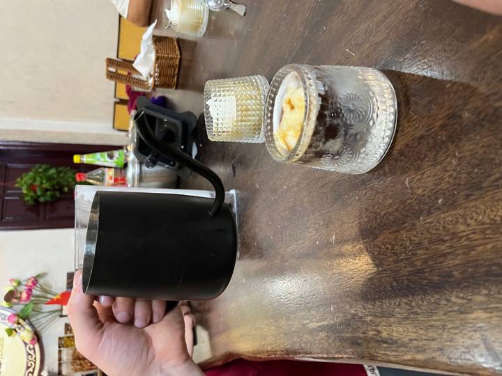 Schwarze Kanne wird neben Glastassen mit einem Dessert ausgegossen.