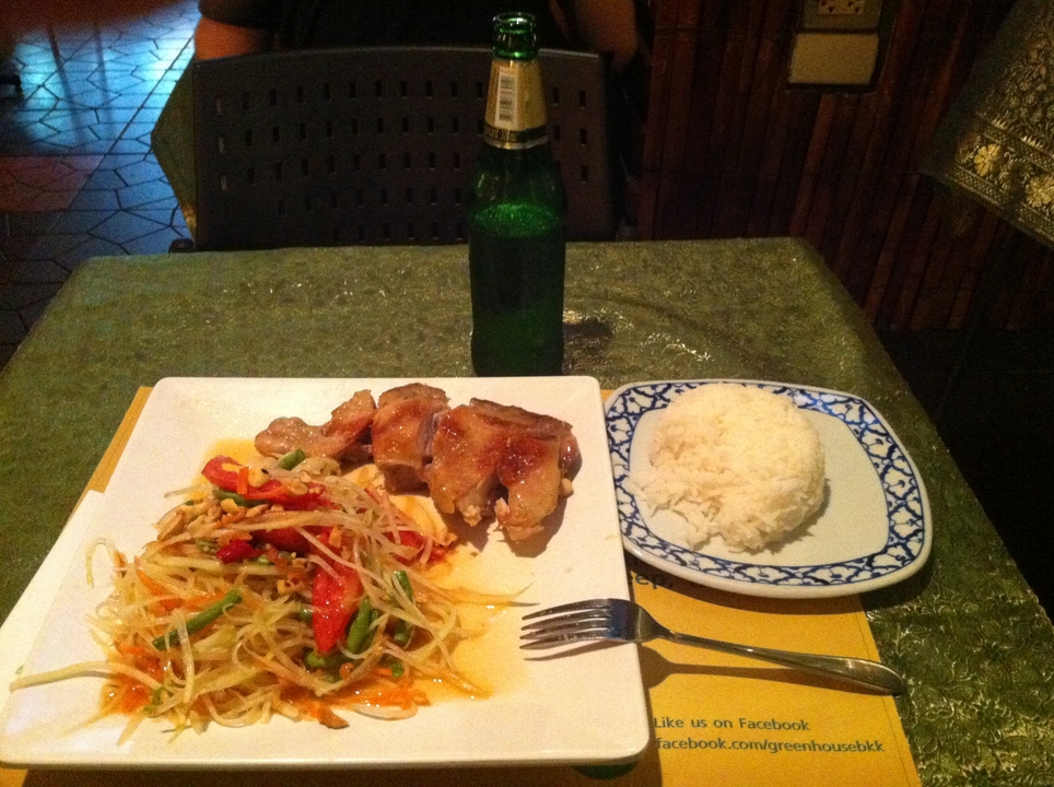 Dinner plate with spicy papaya salad, grilled chicken, rice and beer on a green tablecloth.