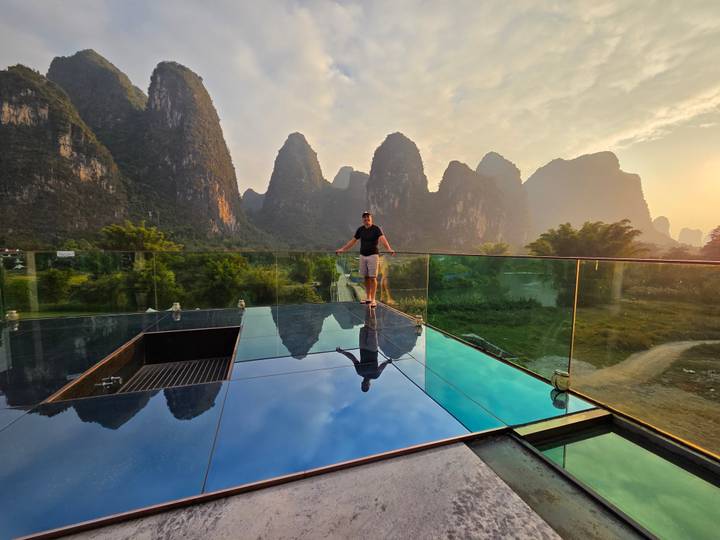 Person standing on a glass platform with scenic mountainous background.