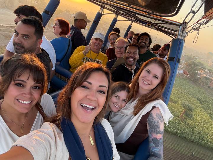 Group of people in a hot air balloon over greenery.