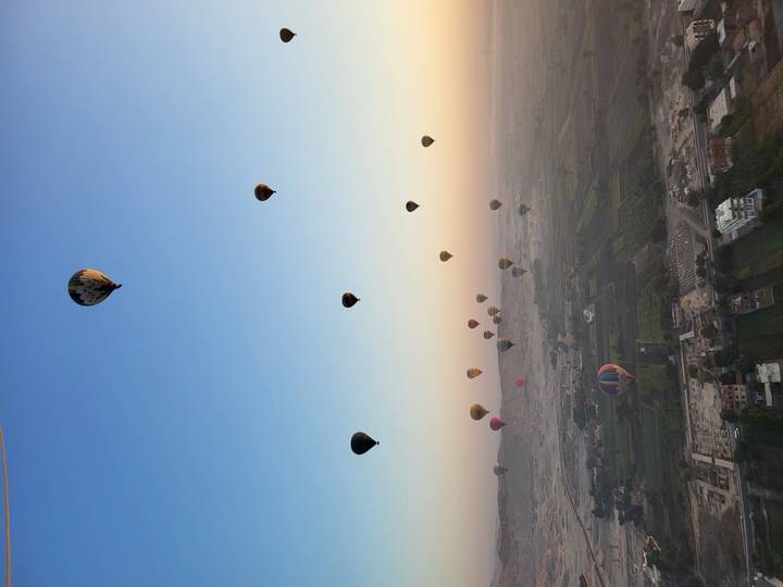 Numerous hot air balloons floating over the landscape during sunrise.