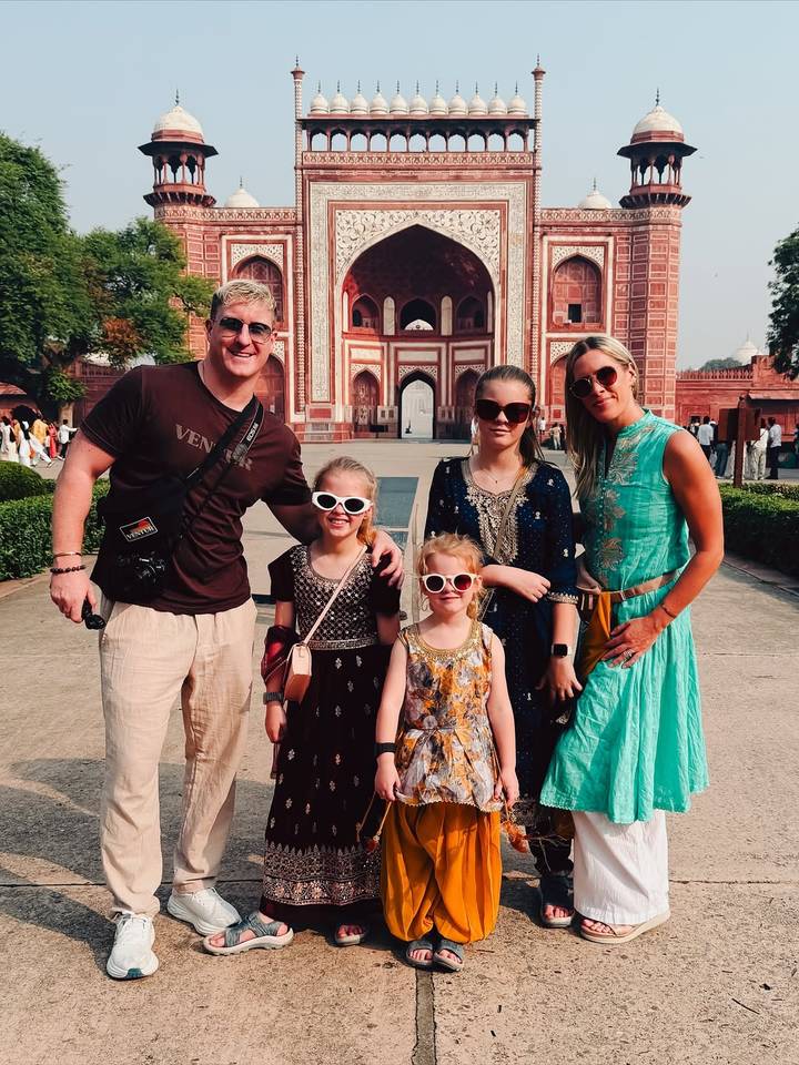 A family in front of a red sandstone entrance gate in a Mughal architectural style.