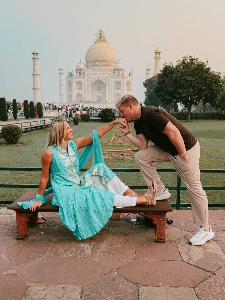 A couple in a romantic pose near the gardens with the Taj Mahal in the background.