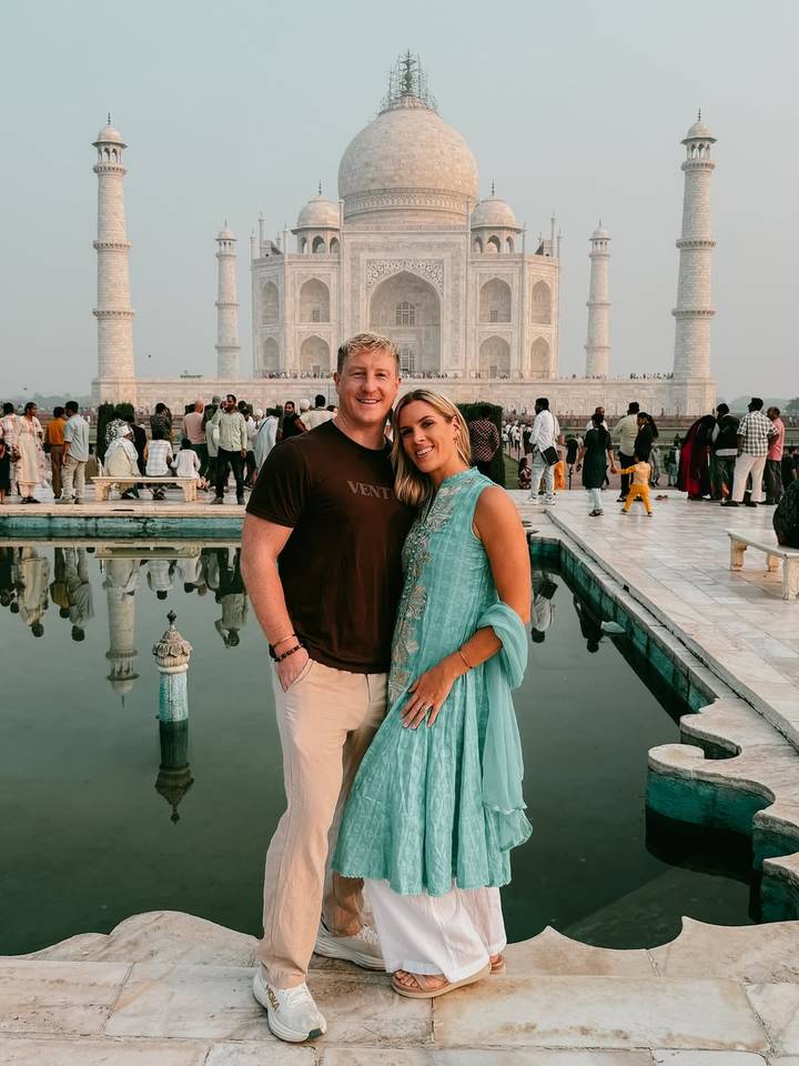 A couple posing in front of a reflecting pool with the Taj Mahal in the background.