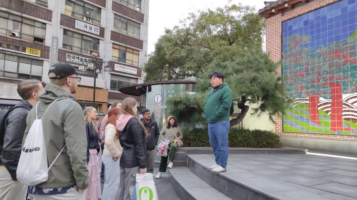 Rondleidingsgroep met een gids voor een muurschildering en stadsgebouwen.