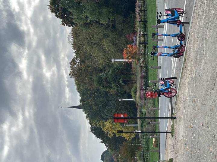Ein Park mit Elektrorollern und einem hohen Turm im Hintergrund.