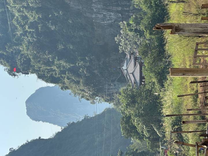 Pavillon chinois traditionnel entouré de verdure luxuriante et de montagnes.