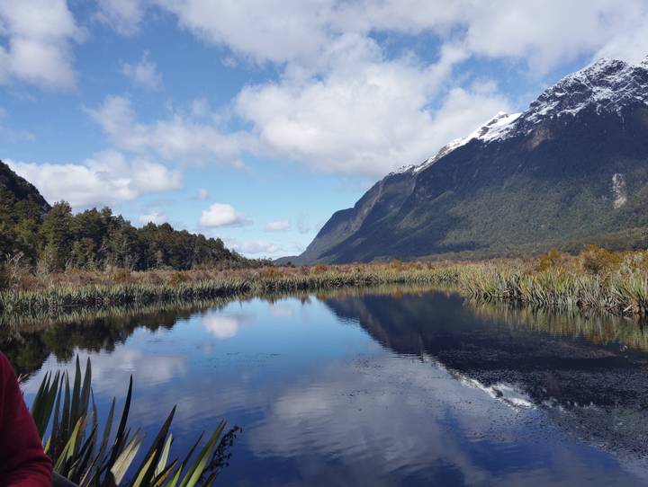 Lago tranquilo con reflejos de montañas y cielo azul.