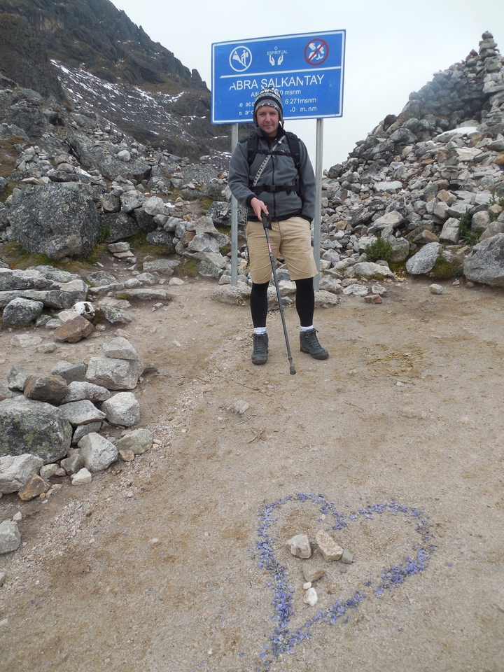 Jambes d'une personne et bâton de randonnée sur un sol rocailleux.