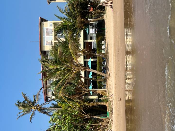 Hotelgebäude mit Palmen an einem Sandstrand.