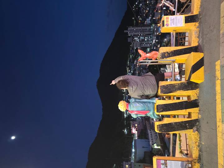 Persoon die buiten zit met twee standbeelden, wijzend naar de lucht tijdens de nacht.