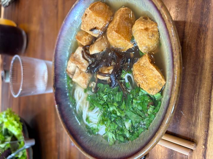 Nahaufnahme einer Schüssel vietnamesischer Nudelsuppe mit Kräutern und Tofu.