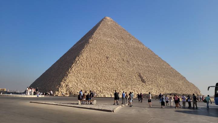 Die Große Pyramide von Gizeh mit Touristen, die bei klarem Himmel um sie herumgehen.