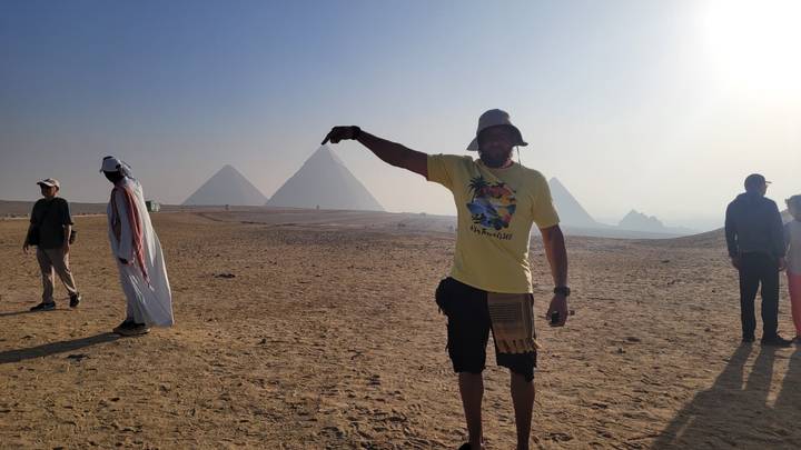 Ein Mann posiert so, als würde er die Spitze einer Pyramide berühren.