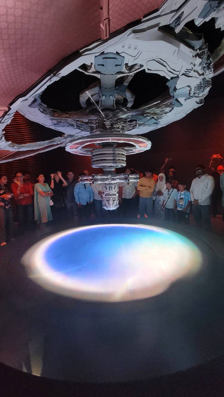 Eine Gruppe von Personen, die um eine Vitrine mit einem schwebenden Objekt darin herumstehen.