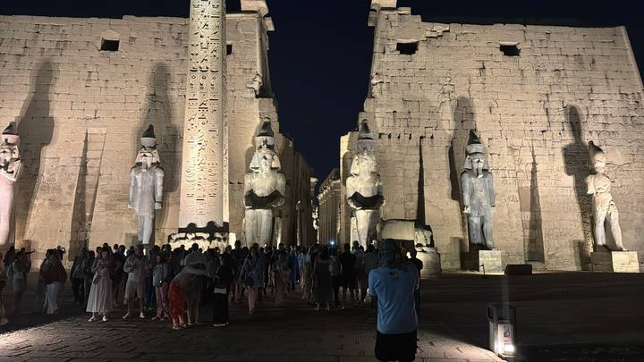 Menschenmenge am Eingang des Luxor-Tempels mit beleuchteten Statuen unter dem Nachthimmel.