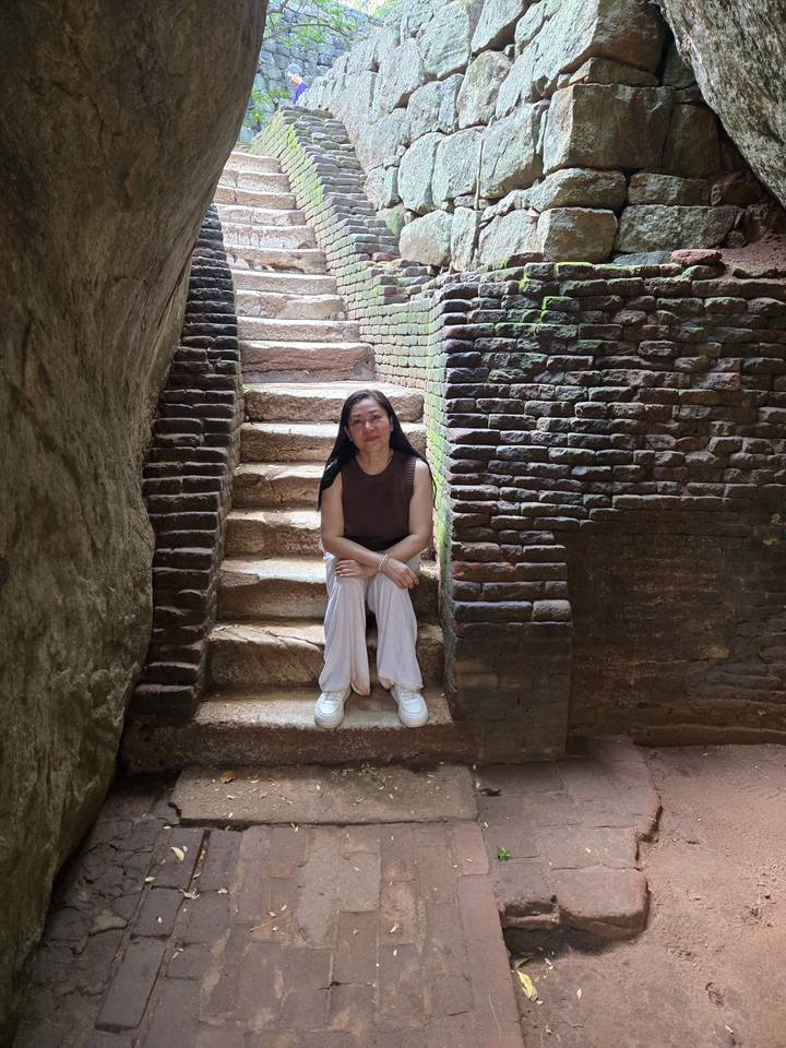 Una mujer sentada en escalones de piedra entre paredes de ladrillo.