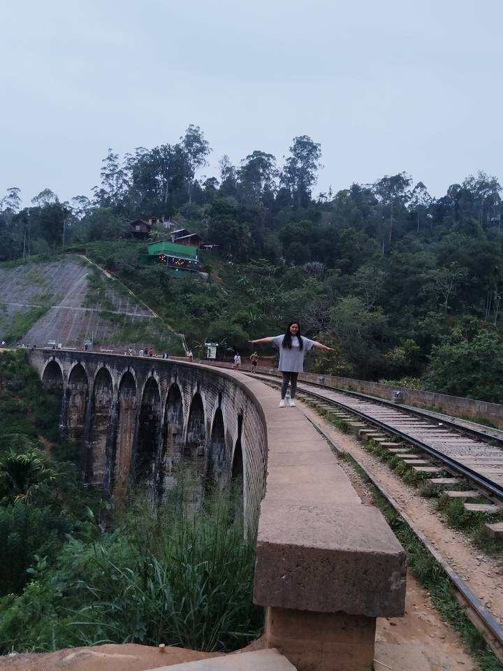 Una mujer parada en una vía férrea sobre un puente.