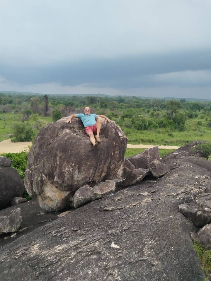 Un hombre reclinado sobre una roca grande con vegetación en el fondo.