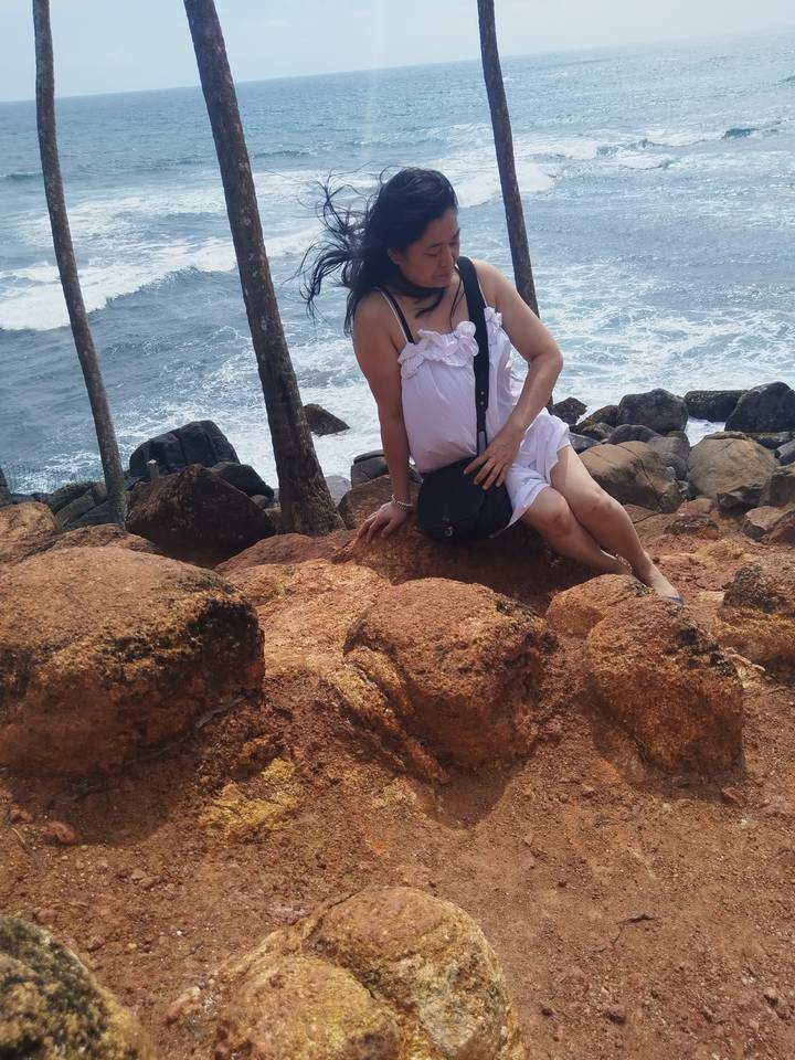 Una mujer posando en la orilla rocosa con olas.