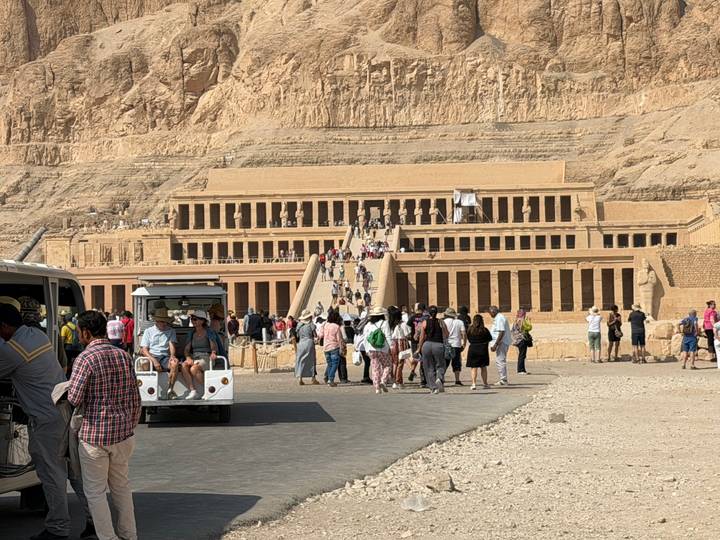 Gran templo egipcio antiguo con turistas y un carrito de golf.