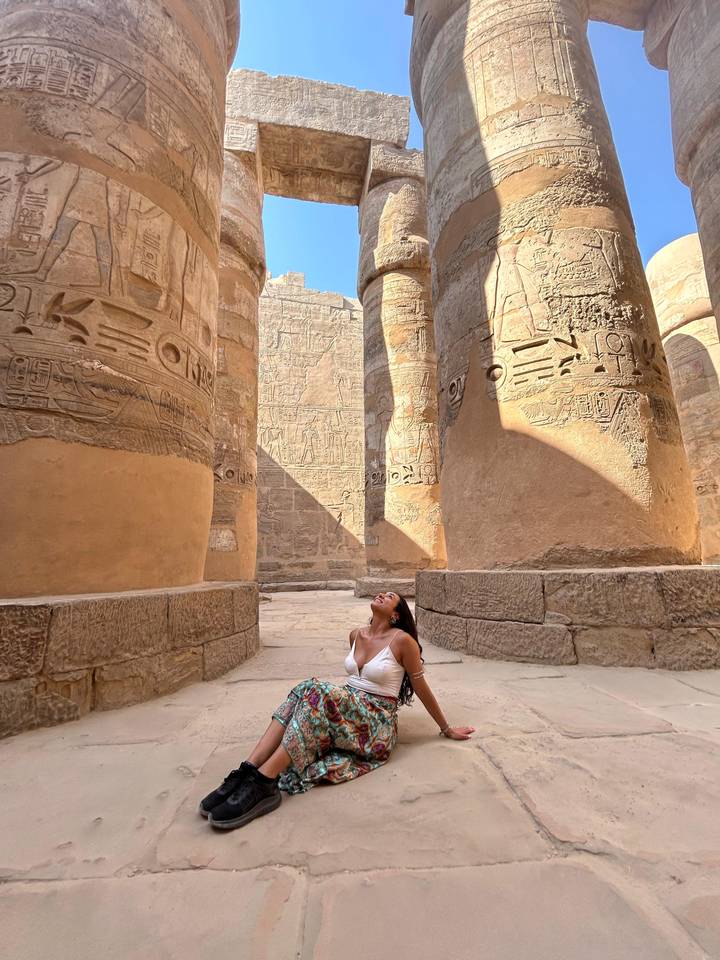 Eine Frau, die zu großen altägyptischen Säulen mit Hieroglyphen aufblickt.