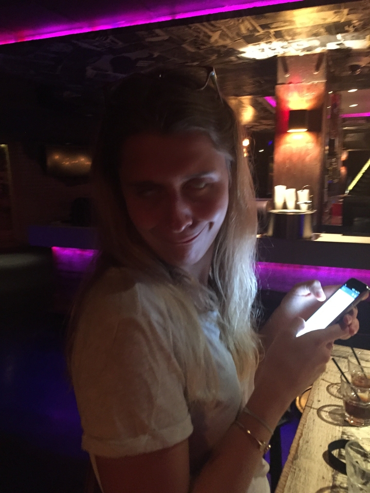 Low-light close-up of a woman making a humorous face while holding a phone.
