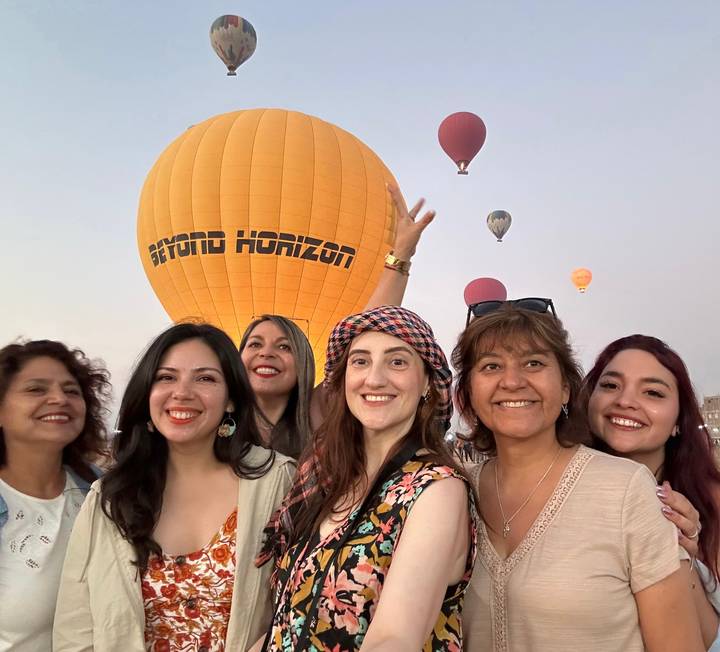 Women posing with hot air balloons in the background.