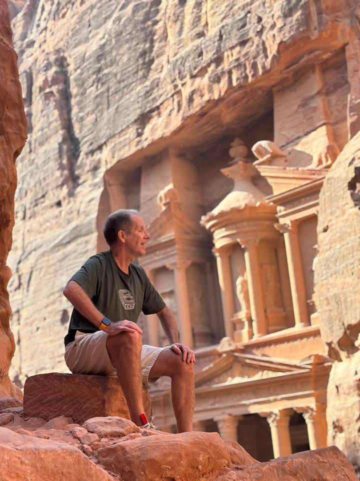 Mann, der vor der ikonischen Schatzkammer von Petra sitzt.