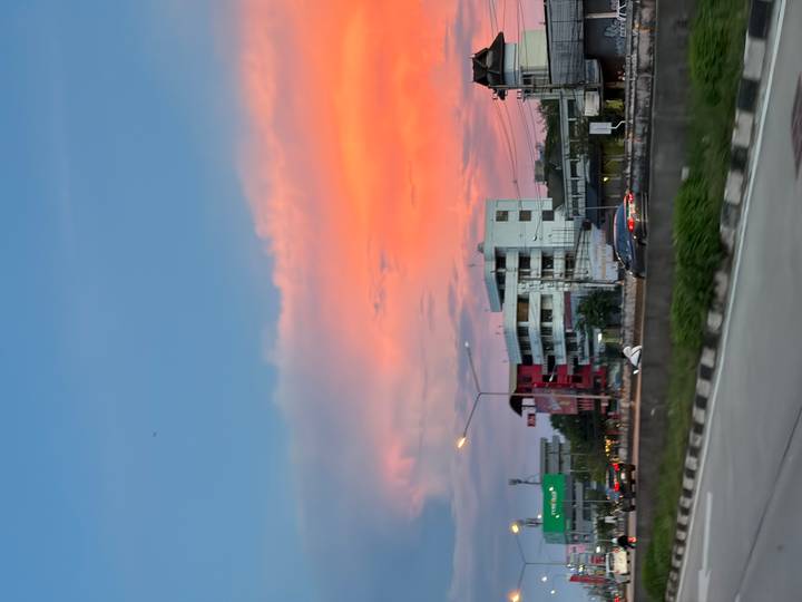 Calle con autos y edificios bajo un cielo colorido de atardecer