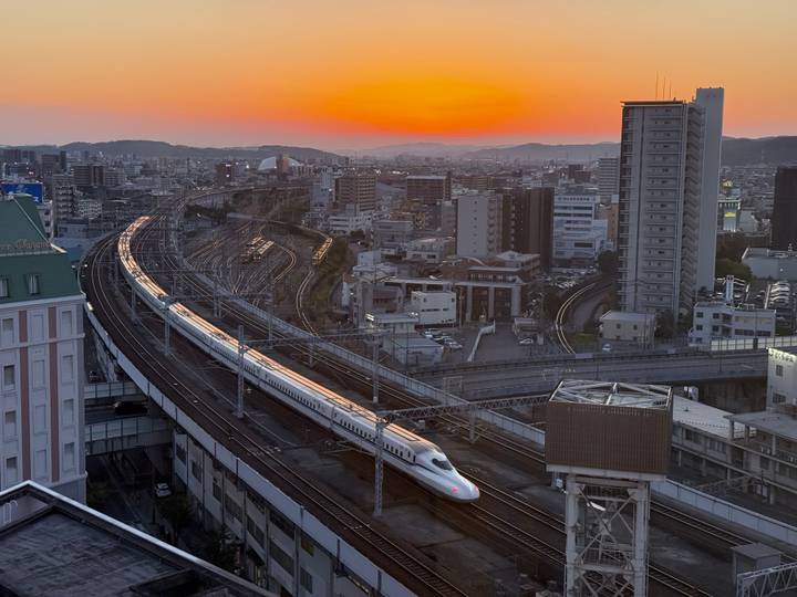 Bullet train moving through a city at sunset.